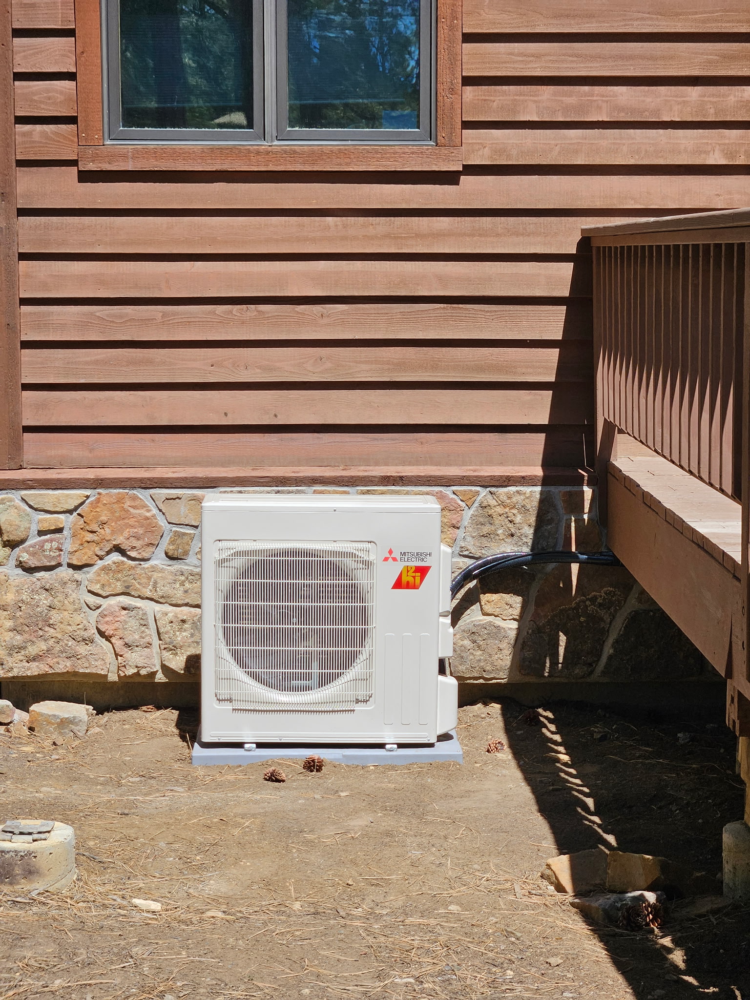 Mini-split outdoor unit installed beside the deck of a log-sided home