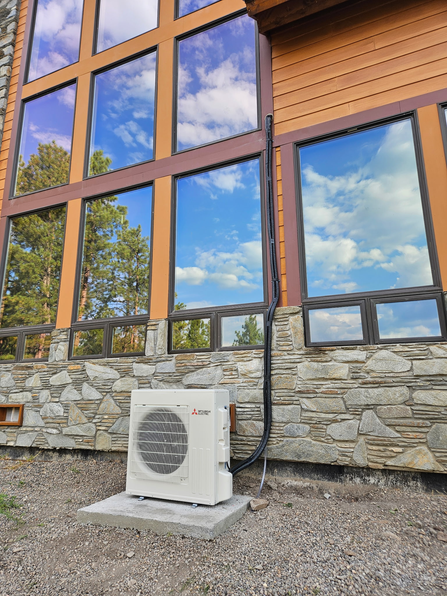 Mini-split outdoor unit on a concrete pad beside a stone and timber mountain home