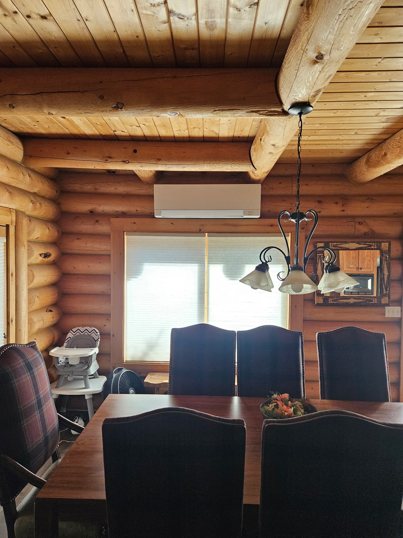 Ductless mini-split indoor unit mounted on a log wall above a dining room window