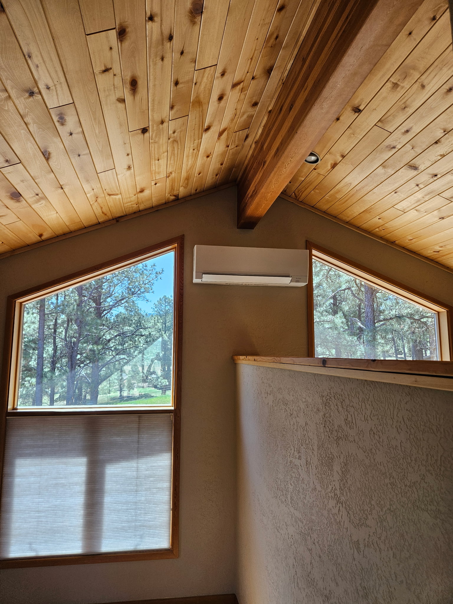 Mini-split indoor unit mounted high on a wall under a vaulted tongue and groove pine ceiling