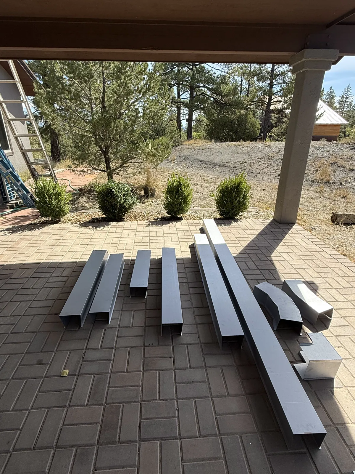 Custom fabricated sheet metal line set cover sections and elbows laid out on a patio before installation